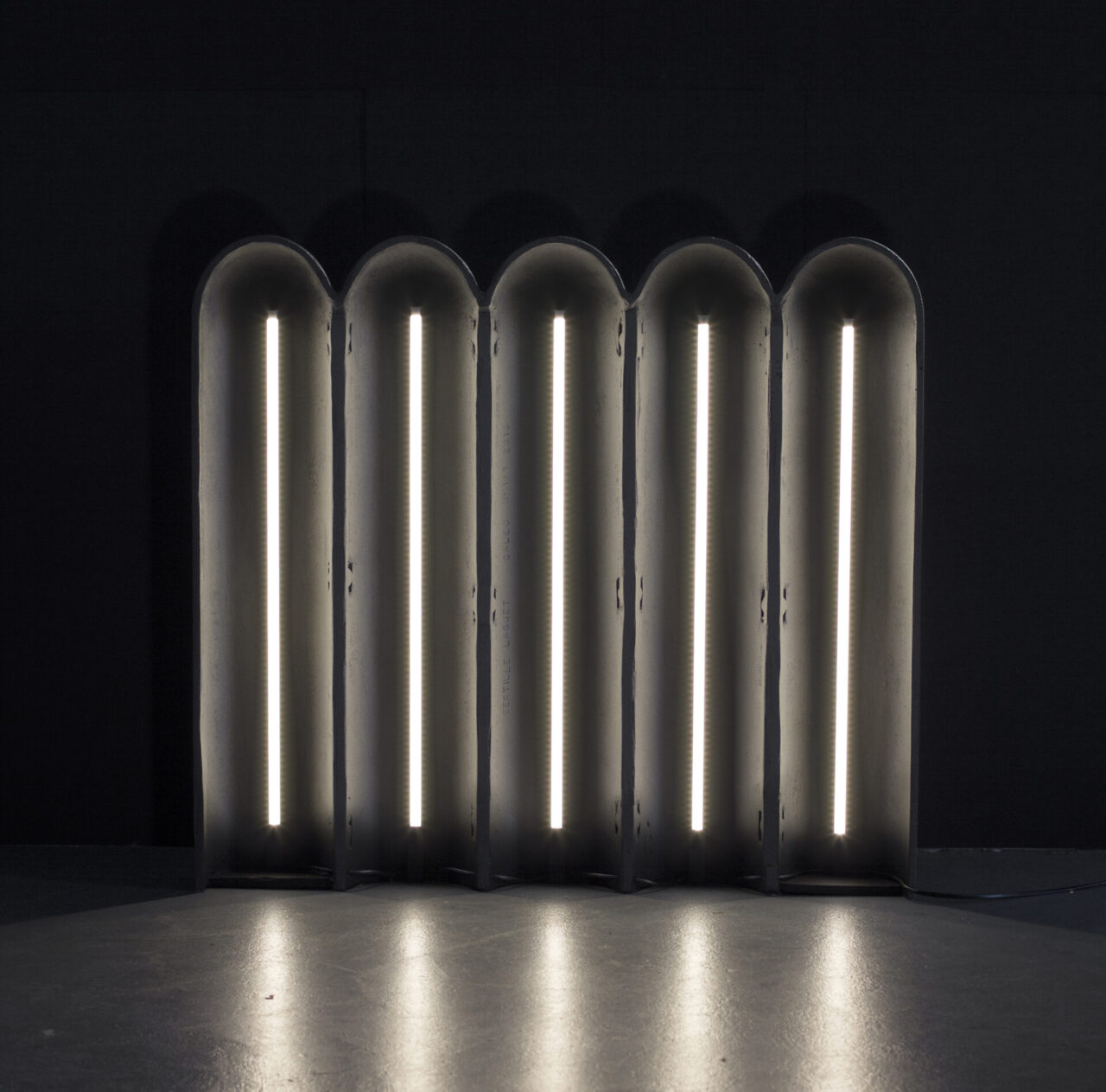 Caleo : envers de l'objet lumineux allumé. Barres LED et fonderie d'aluminium gris anthracite. Design suisse Bertille Laguet. Fabrication française par l'artiste elle-même.