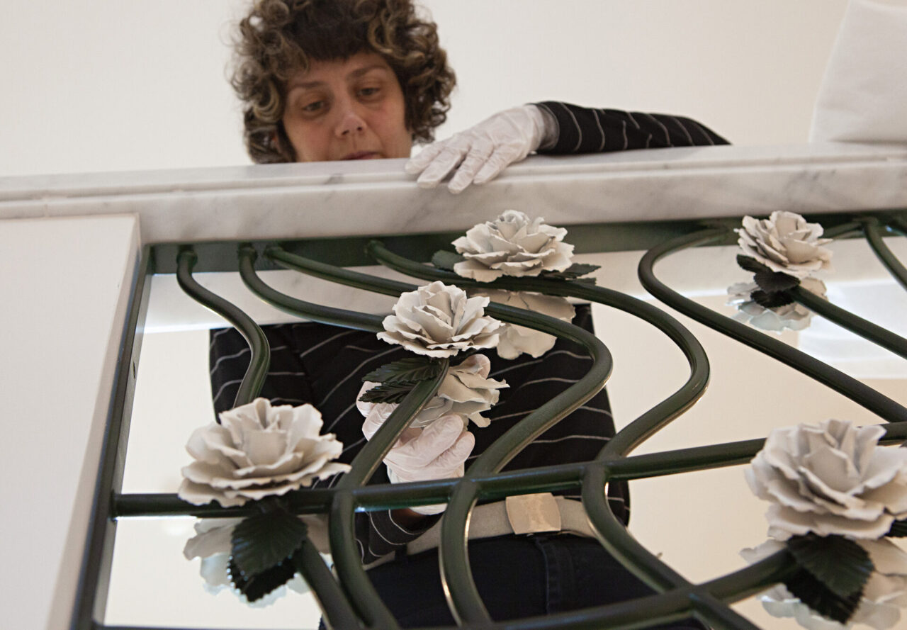 La roseraie : Bertille Laguet ajuste les dernières roses de la rampe d'escalier en fer forgé vert foncé garni de roses blanches. Design et fabrication Bertille Laguet